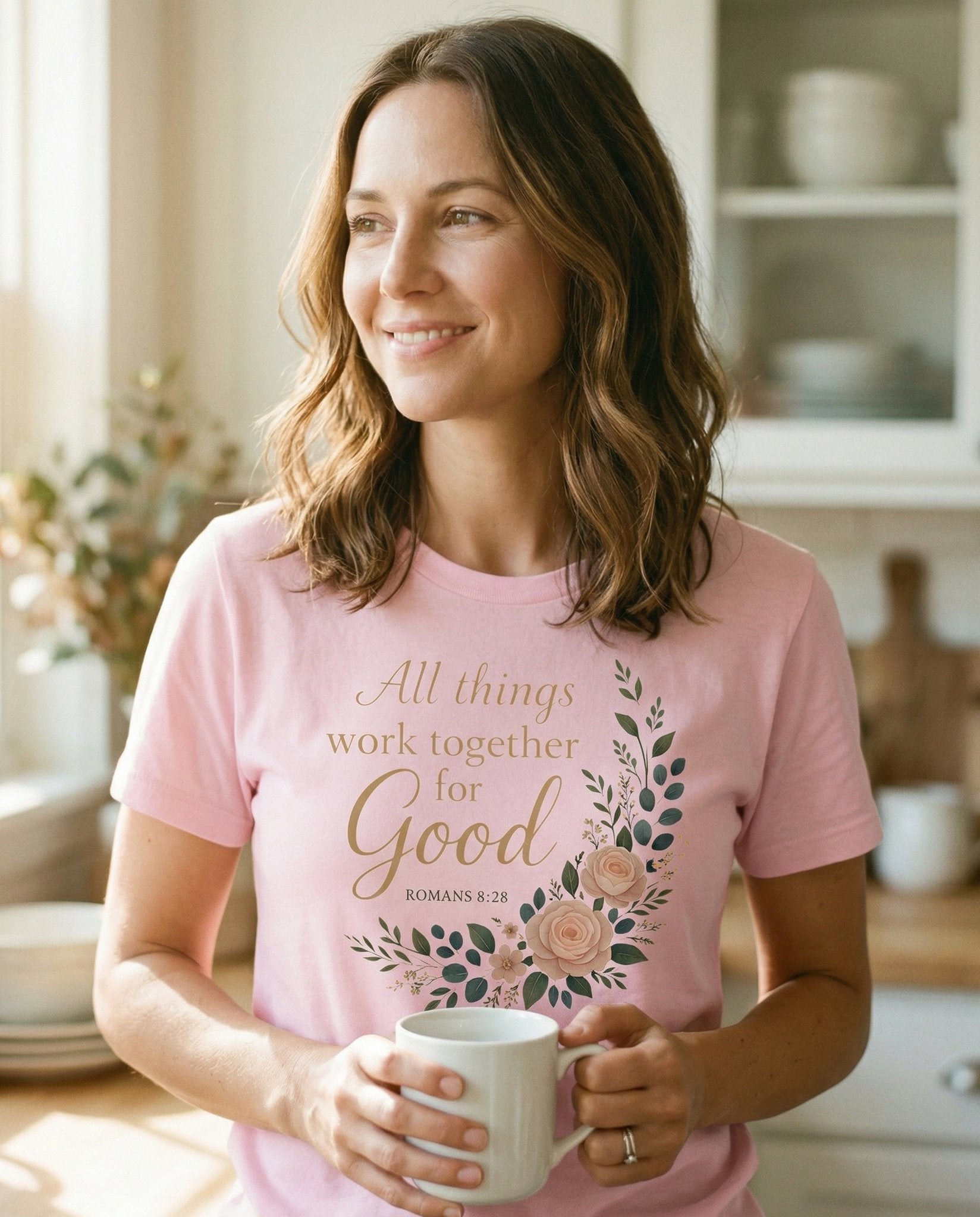 All Things Work Together for Good T-shirt – Blossom women's Christian tee, lifestyle photo in morning kitchen setting – Watercolor floral wreath with blush roses and green leaves framing the – Romans 8:28 – She Wears Faith