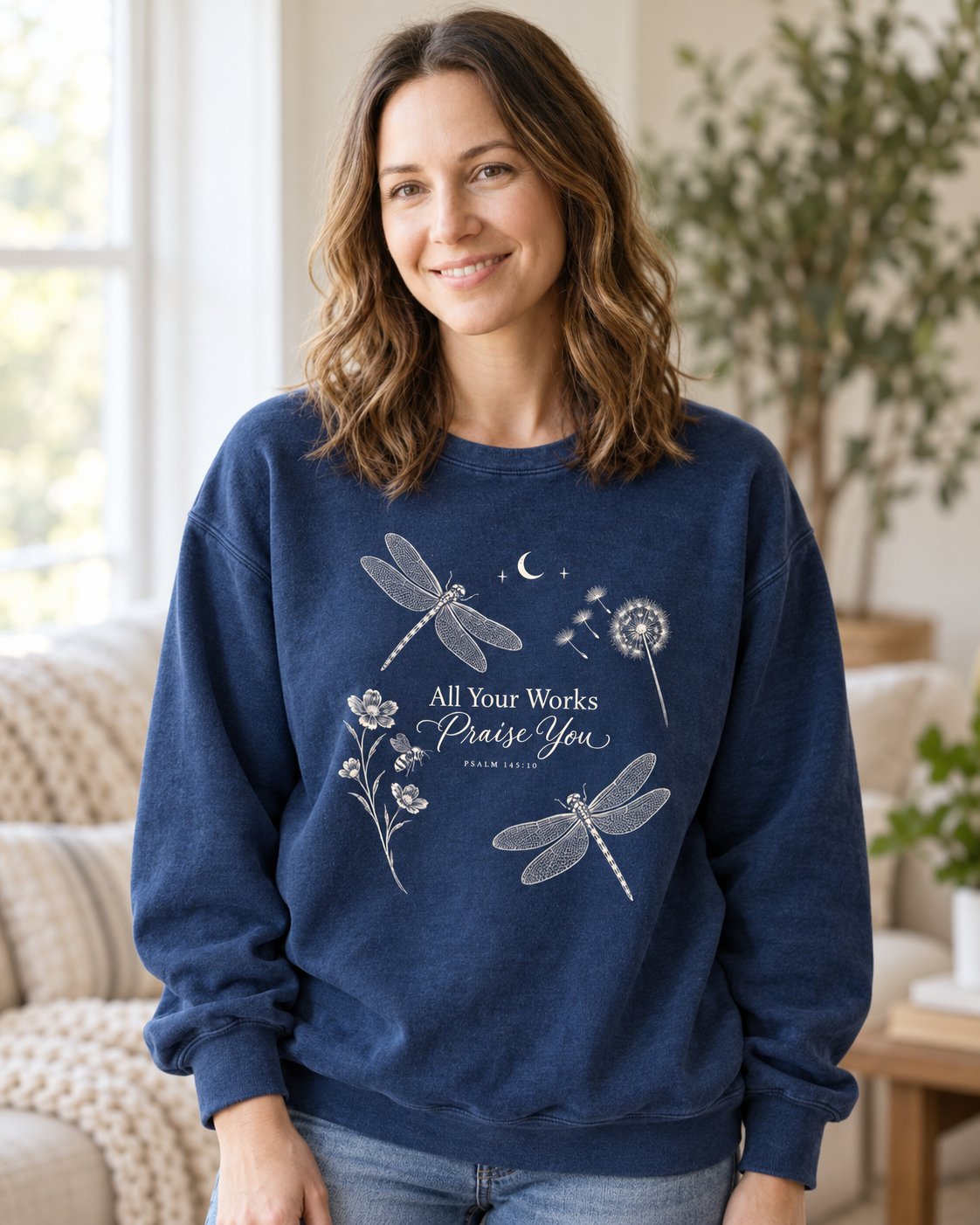 All Your Works Praise You, True Navy women's Christian sweatshirt, lifestyle photo in cozy living room, Dragonflies and wildflowers around All Your Works Praise You script, She Wears Faith