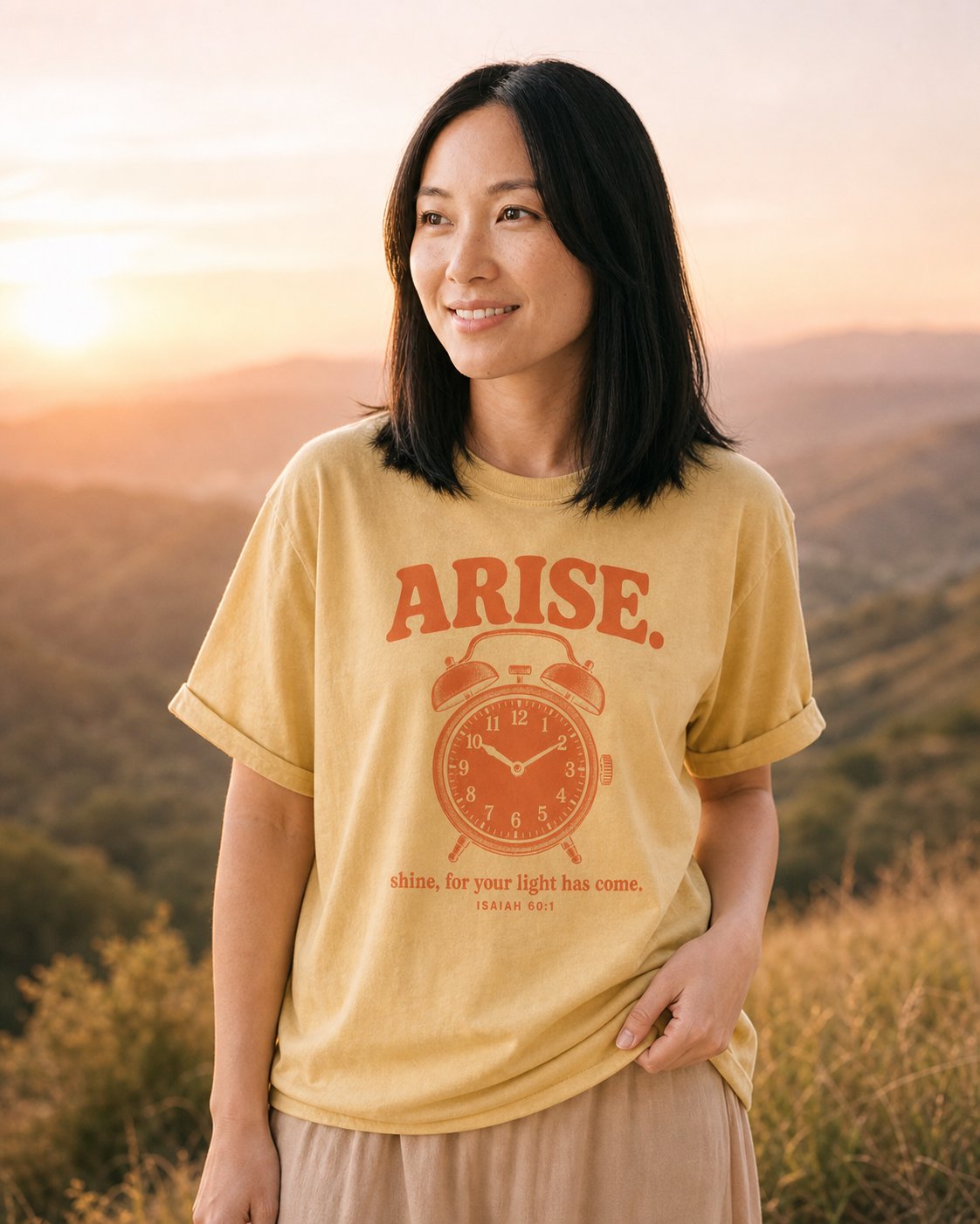 Arise and Shine Isaiah 60:1 – Butter women's Christian tee, lifestyle photo in wildflower meadow at sunrise – Retro alarm clock with bold ARISE lettering – Isaiah 60:1 – She Wears Faith