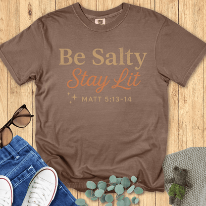 Espresso brown Comfort Colors 1717 shirt with the Christian message “Be Salty Stay Lit – Matt 5:13-14,” styled flat lay with casual wear