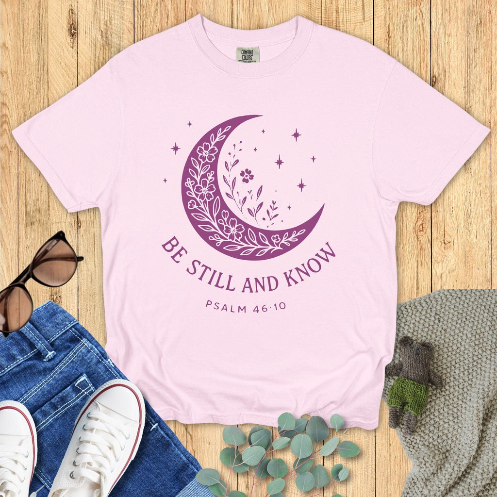 Comfort Colors Christian T-shirt in soft blossom pink, decorated with a purple crescent moon, floral accents, and stars, with the verse “Be Still and Know – Psalm 46:10.”
