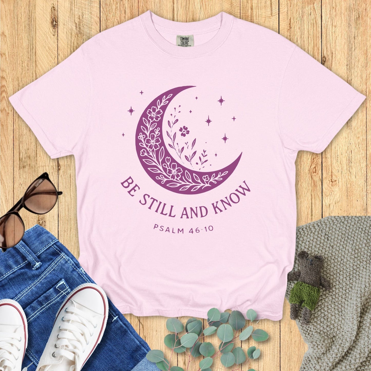 Comfort Colors Christian T-shirt in soft blossom pink, decorated with a purple crescent moon, floral accents, and stars, with the verse “Be Still and Know – Psalm 46:10.”