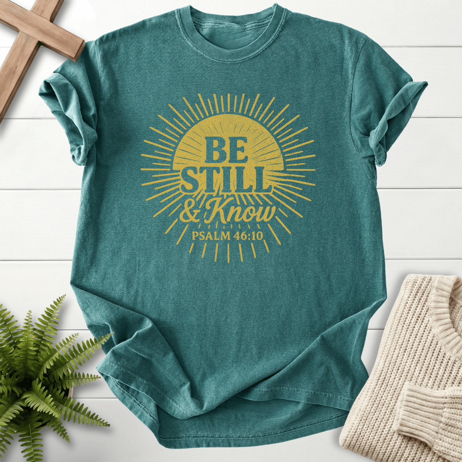 Blue Spruce Christian t-shirt for women with a bold gold sunburst graphic and 'Be Still and Know', inspired by Psalm 46:10.