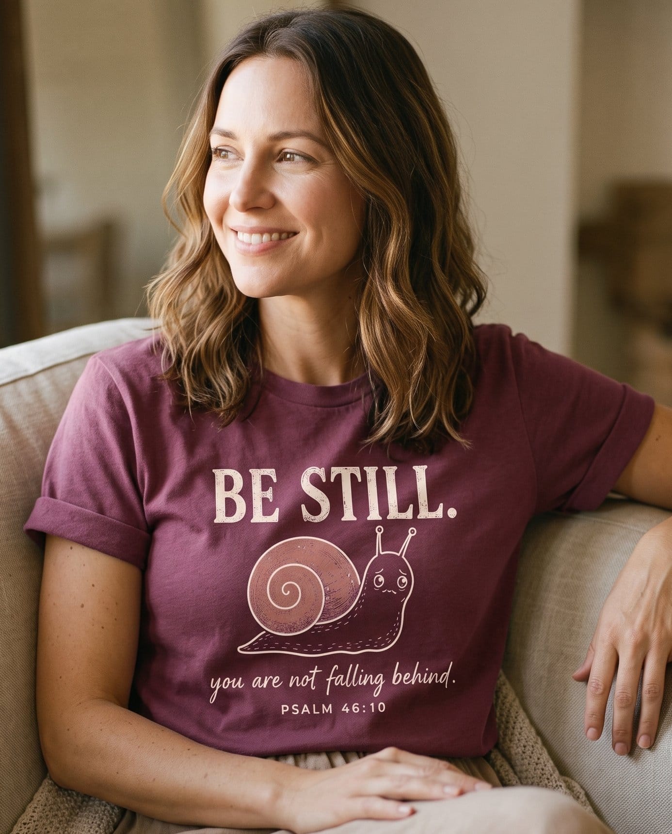Be Still Snail Ps 46:10 – Berry women's Christian tee, lifestyle photo in cozy living room – BE STILL – Psalm 46:10 – She Wears Faith