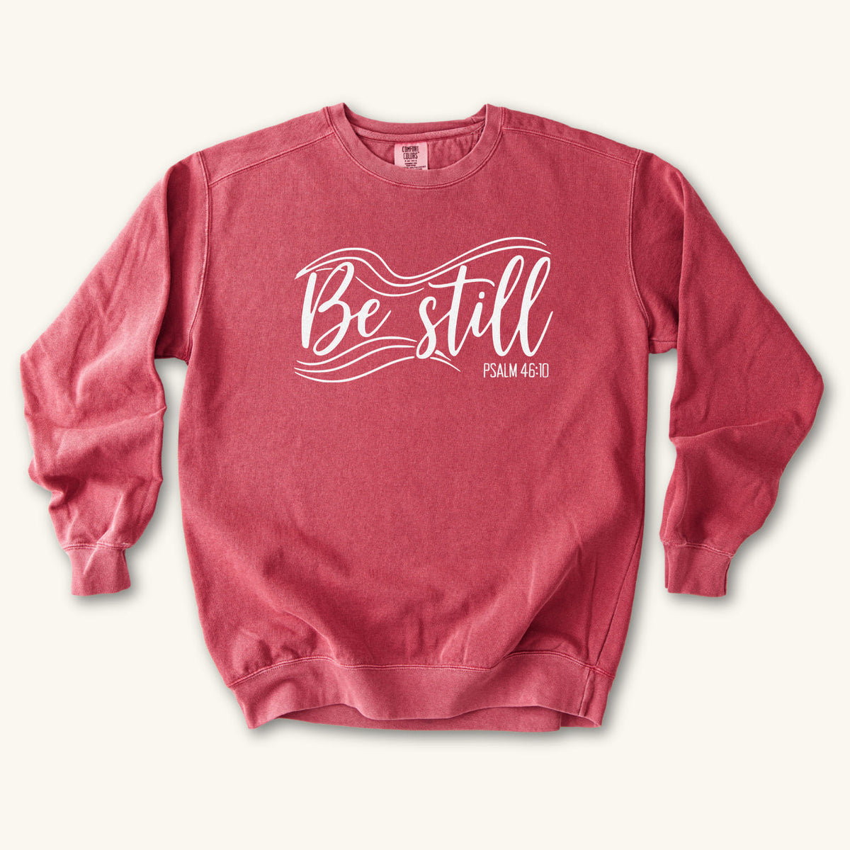 Crimson Christian sweatshirt reading Be still in flowing brush script with sweeping lines, Psalm 46:10