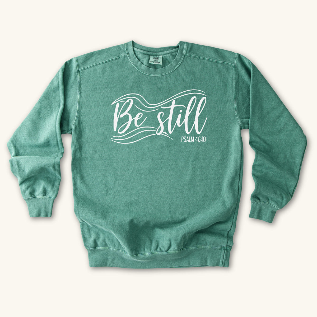 Light Green Christian sweatshirt reading Be still in flowing brush script with sweeping lines, Psalm 46:10