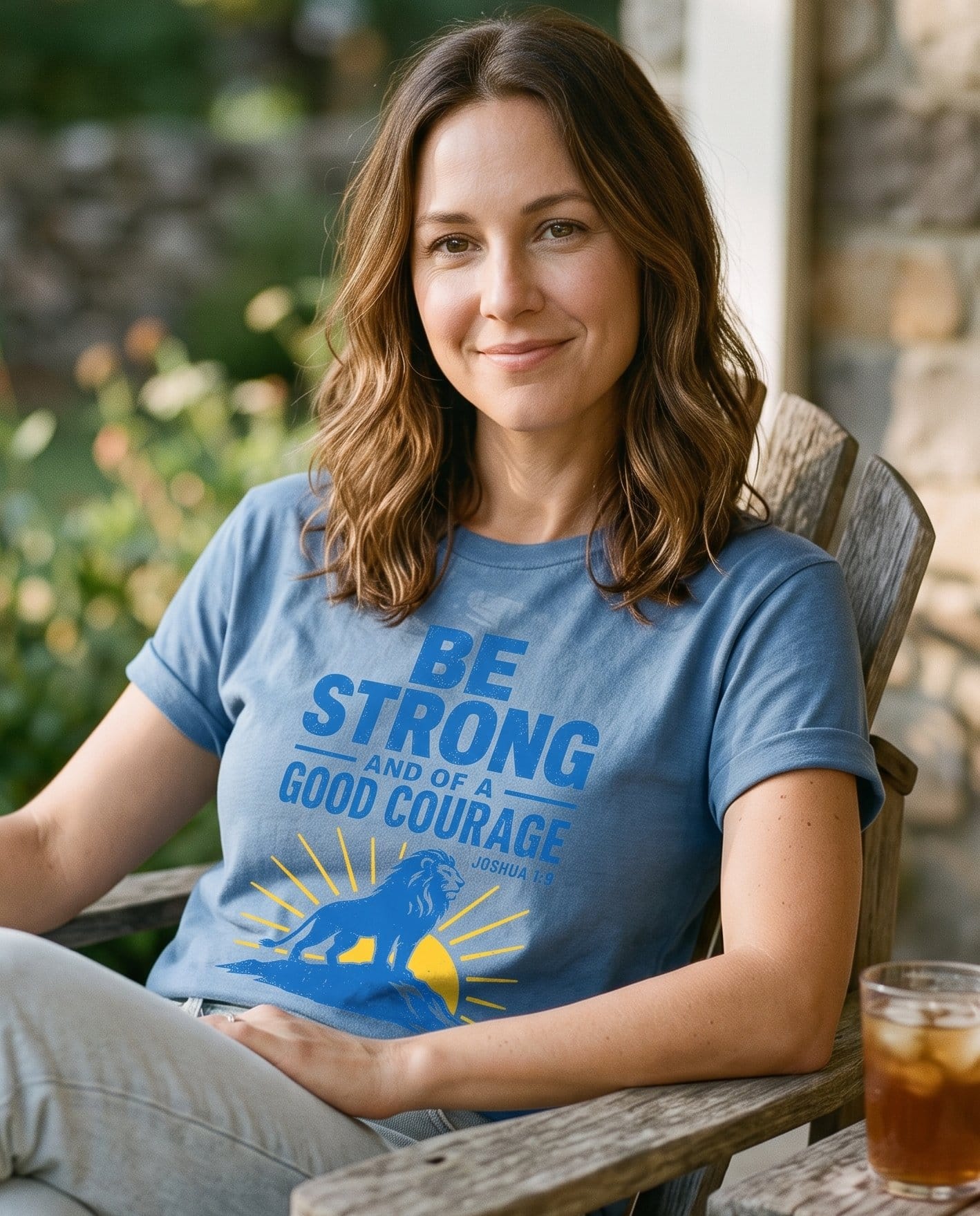 Be Strong and of a Good Courage Joshua 1:9 Lion – Blue Jean women's Christian tee, lifestyle photo in sunny porch – Bold condensed capital lettering 'Be Strong and of a Good Courage' wit – Joshua 1:9 – She Wears Faith