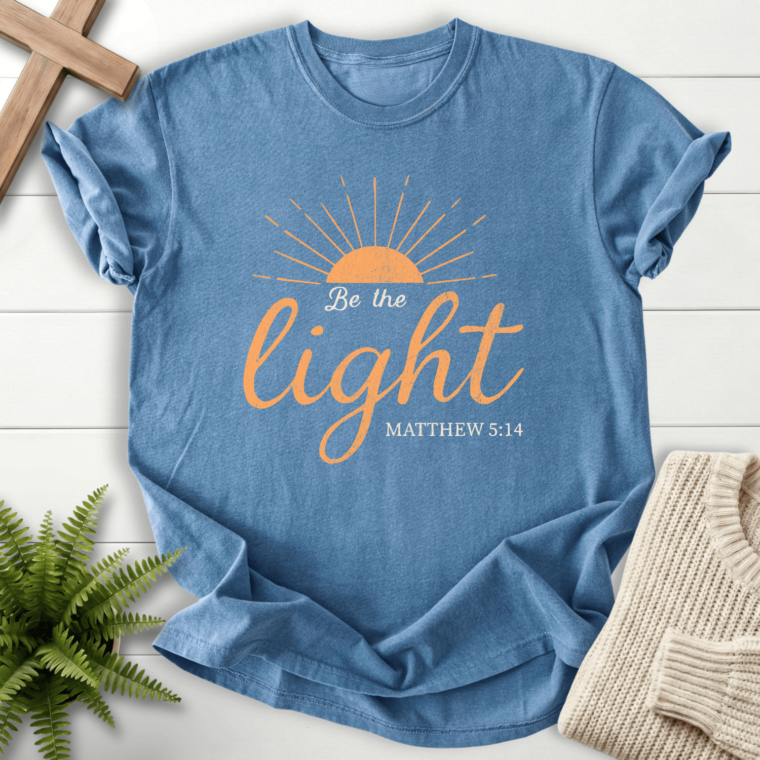 Blue Jean Christian t-shirt for women with a rising sun and script design, 'Be the Light', inspired by Matthew 5:14.