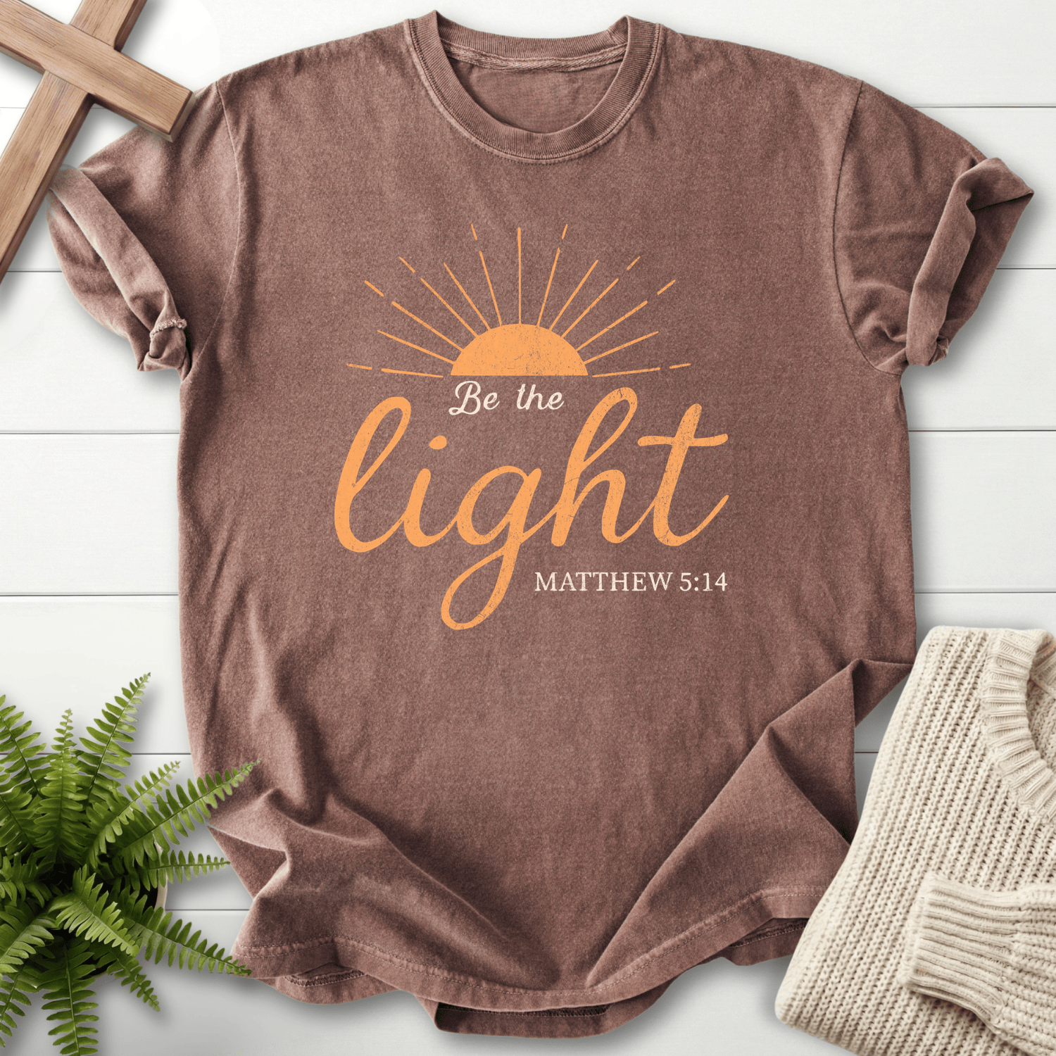 Espresso Christian t-shirt for women with a rising sun and warm orange script, 'Be the Light', inspired by Matthew 5:14.