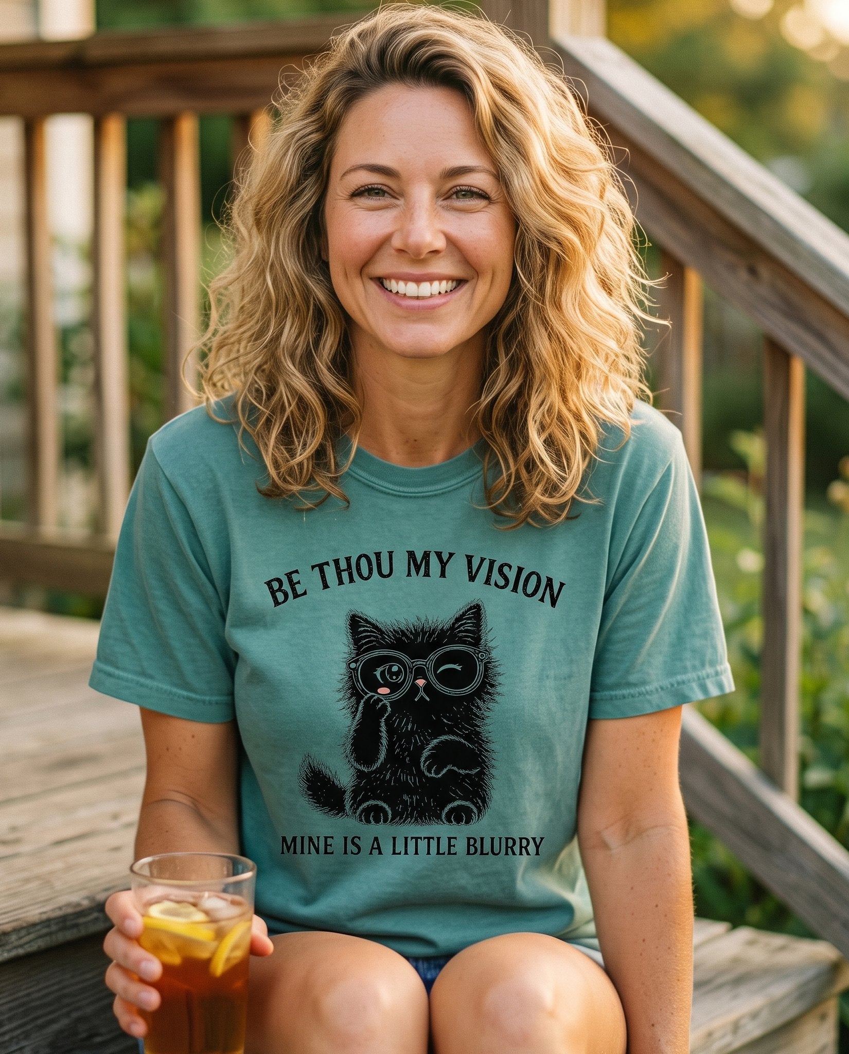 Be Thou My Vision Cat – Chalky Mint women's Christian tee, lifestyle photo in sunny porch – A winking black kitten in round glasses with one paw raised beneath th – Be Thou My Vision (hymn) – She Wears Faith