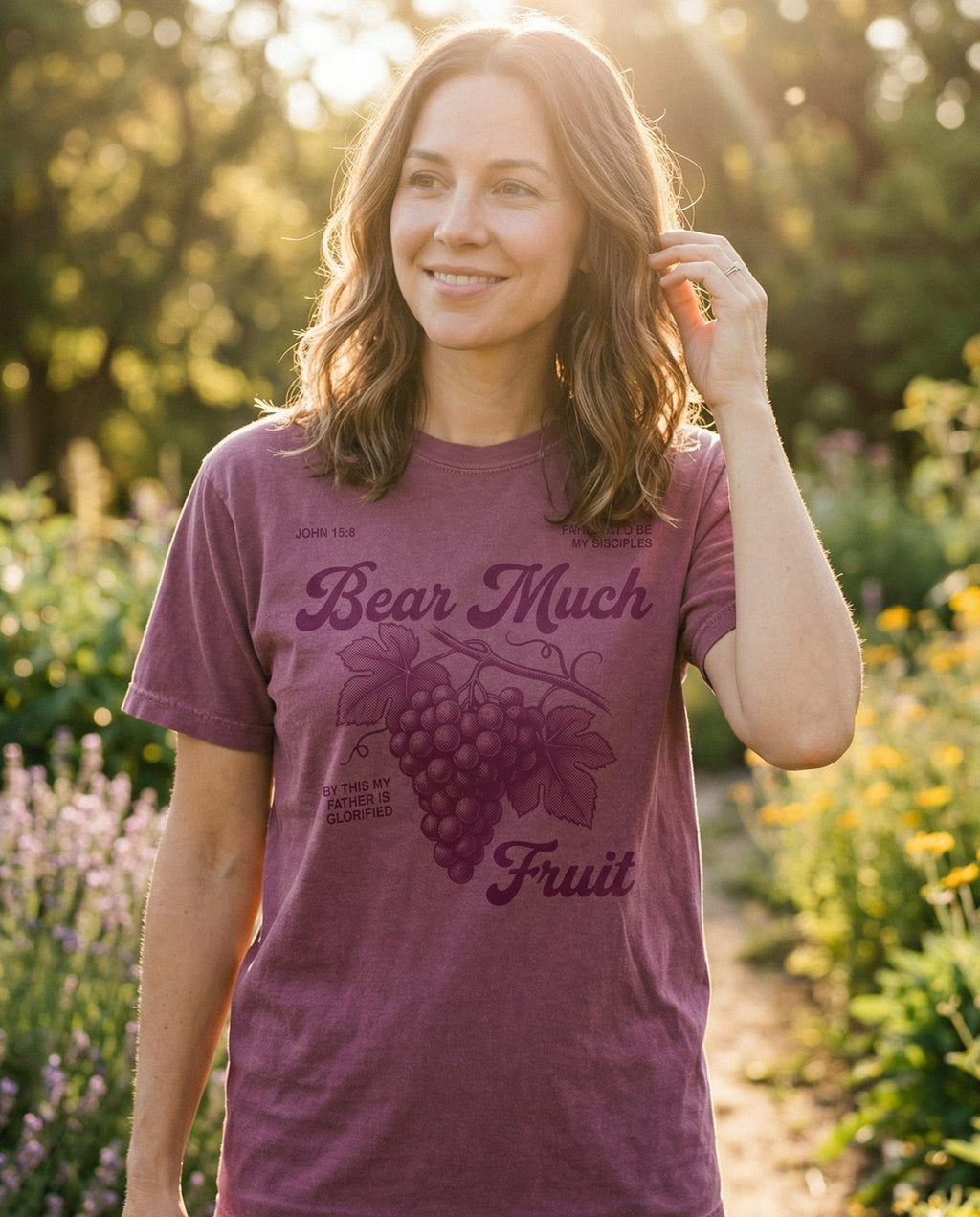 Bear Much Fruit – Berry women's Christian tee, lifestyle photo in outdoor garden – Vintage-style illustration of a grape cluster with leaves and vine – John 15:9 – She Wears Faith