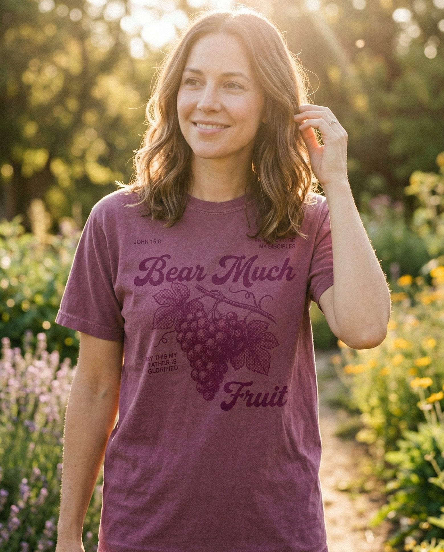 Bear Much Fruit – Berry women's Christian tee, lifestyle photo in outdoor garden – Vintage-style illustration of a grape cluster with leaves and vine – John 15:9 – She Wears Faith