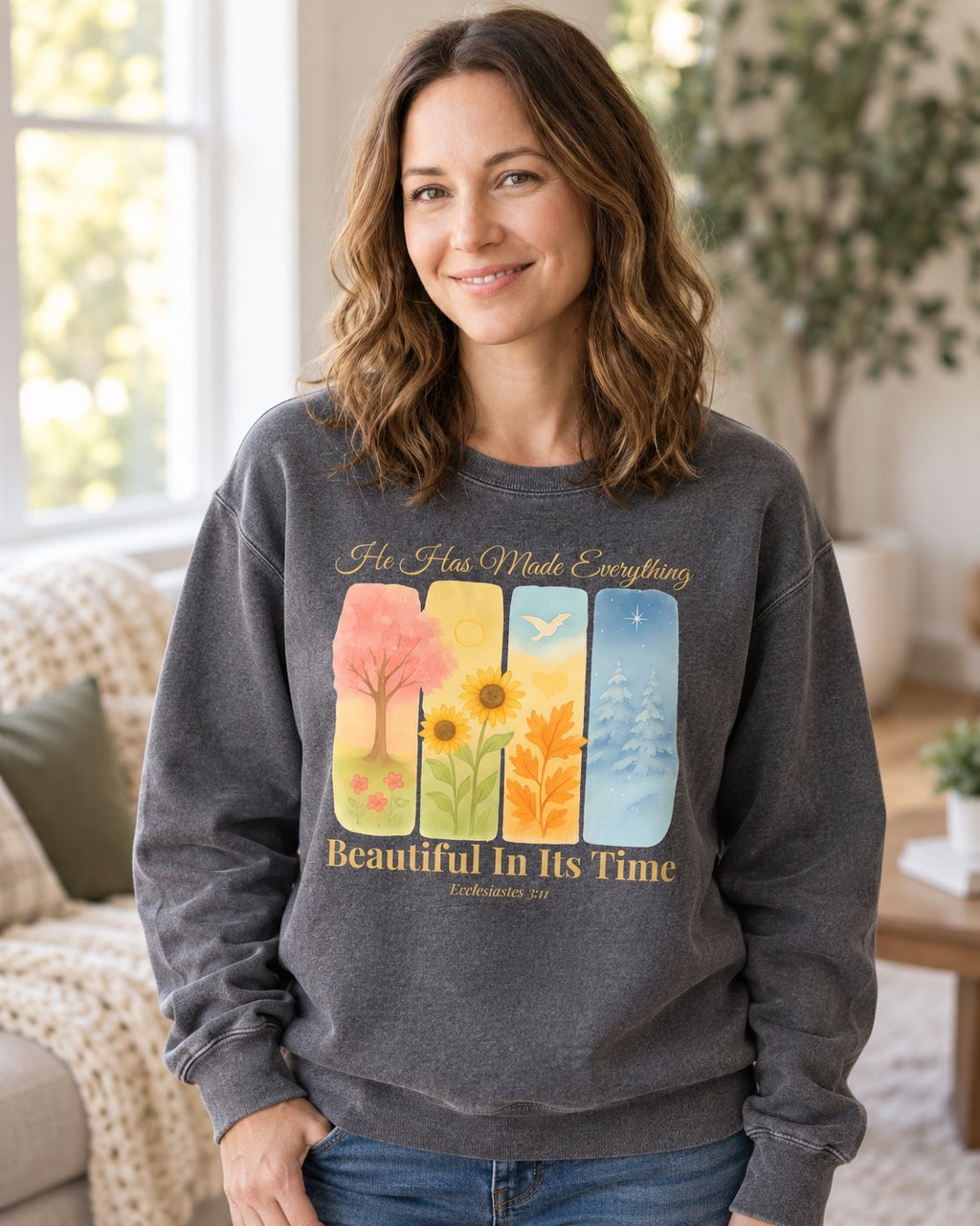 Beautiful In Its Time – Pepper women's Christian sweatshirt, lifestyle photo in cozy living room – Four seasonal tree panels above Beautiful In Its Time – She Wears Faith