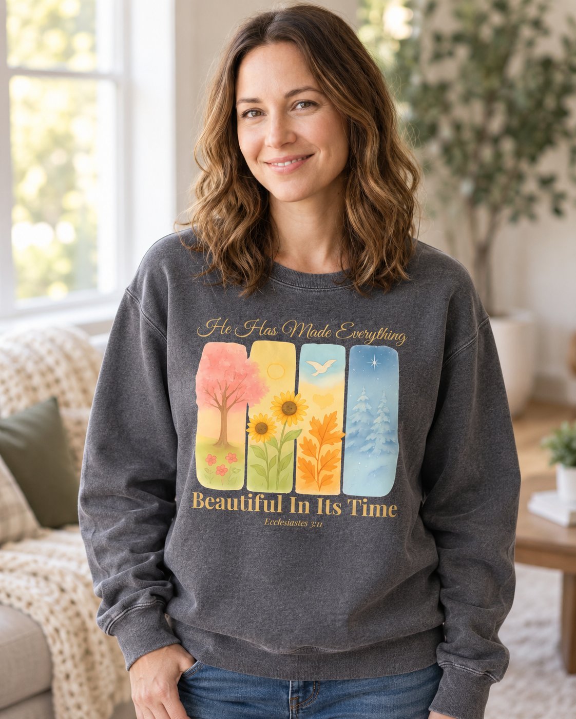Beautiful In Its Time – Pepper women's Christian sweatshirt, lifestyle photo in cozy living room – Four seasonal tree panels above Beautiful In Its Time – She Wears Faith