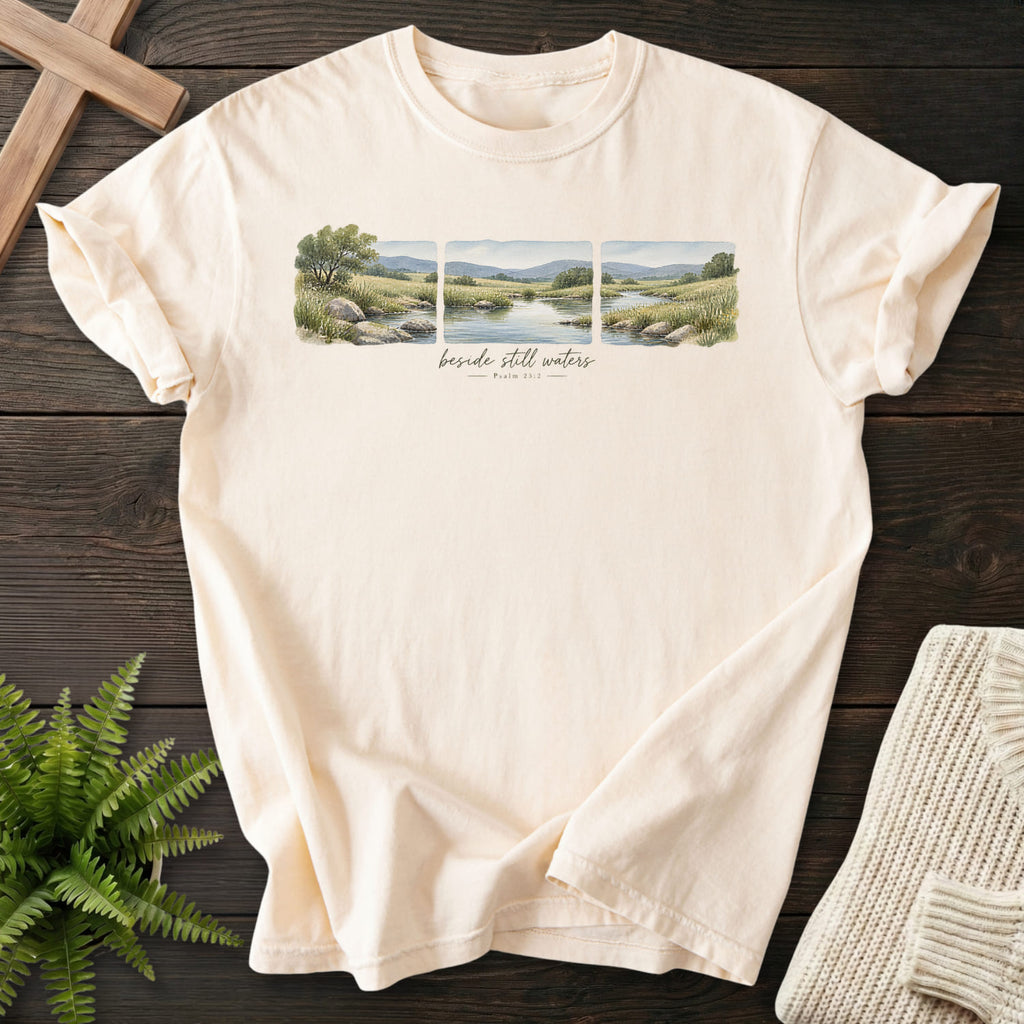 Flat lay of an Ivory Comfort Colors 1717 garment-dyed Christian tee featuring watercolor artwork with "Beside Still Waters T-Shirt" Psalm 23:2.