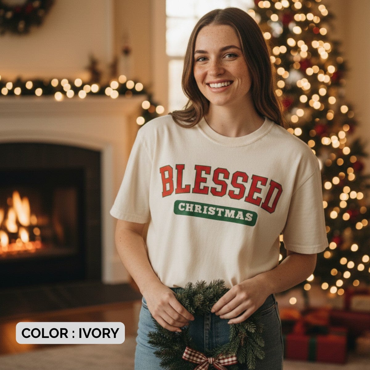 Smiling woman standing near a Christmas tree and fireplace wearing a Comfort Colors 1717 ivory “Blessed Christmas” t-shirt with red and green varsity text. A joyful women’s scripture tee — faith-based apparel for women and modern Christian shirt, meaningful Christian mom gift idea for the holidays.