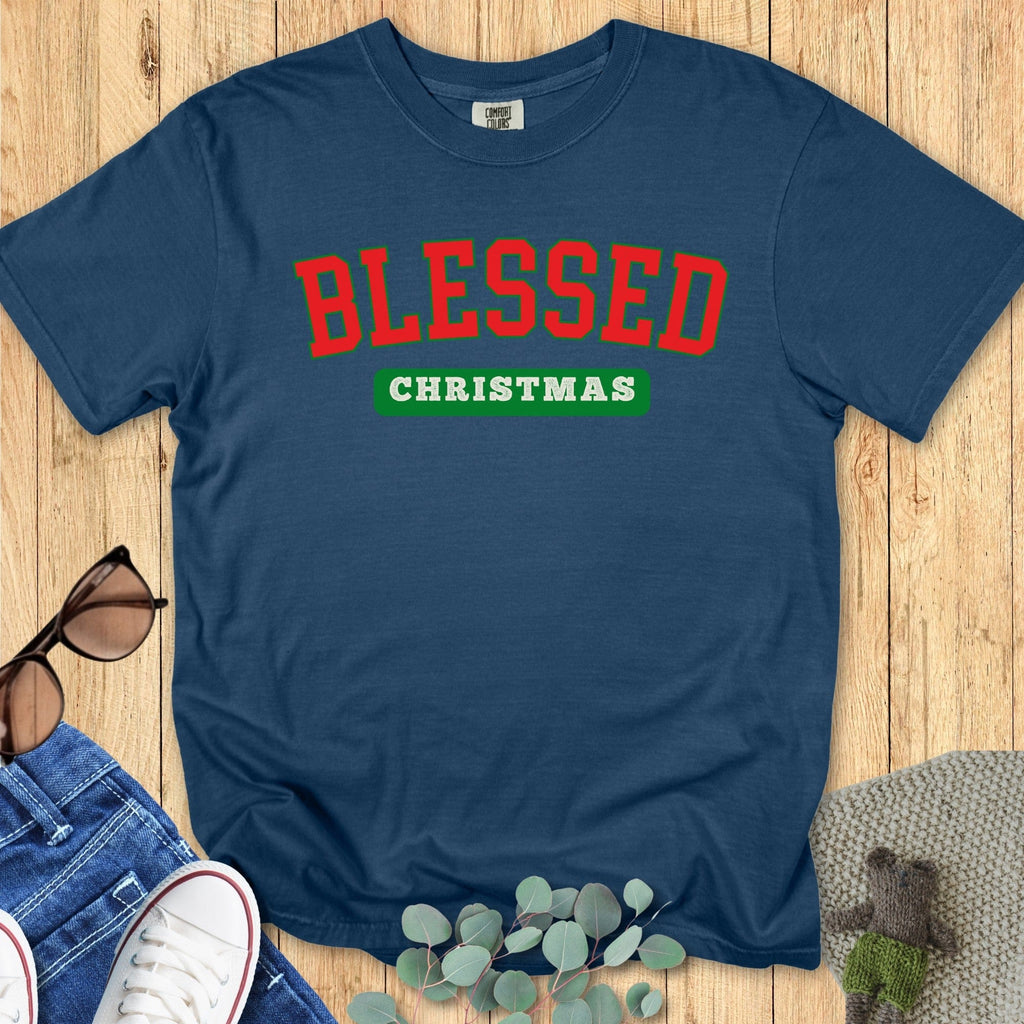 Flatlay of a Comfort Colors 1717 midnight blue “Blessed Christmas” t-shirt with bold red and green varsity lettering. A festive women’s scripture tee — faith-based apparel for women and modern Christian shirt, thoughtful Christian mom gift idea for the holiday season.