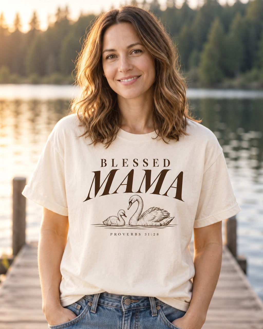 Blessed Mama Swan, Ivory women's Christian tee, lifestyle photo in lakeside setting, Brown BLESSED MAMA lettering with a swan and cygnet, She Wears Faith