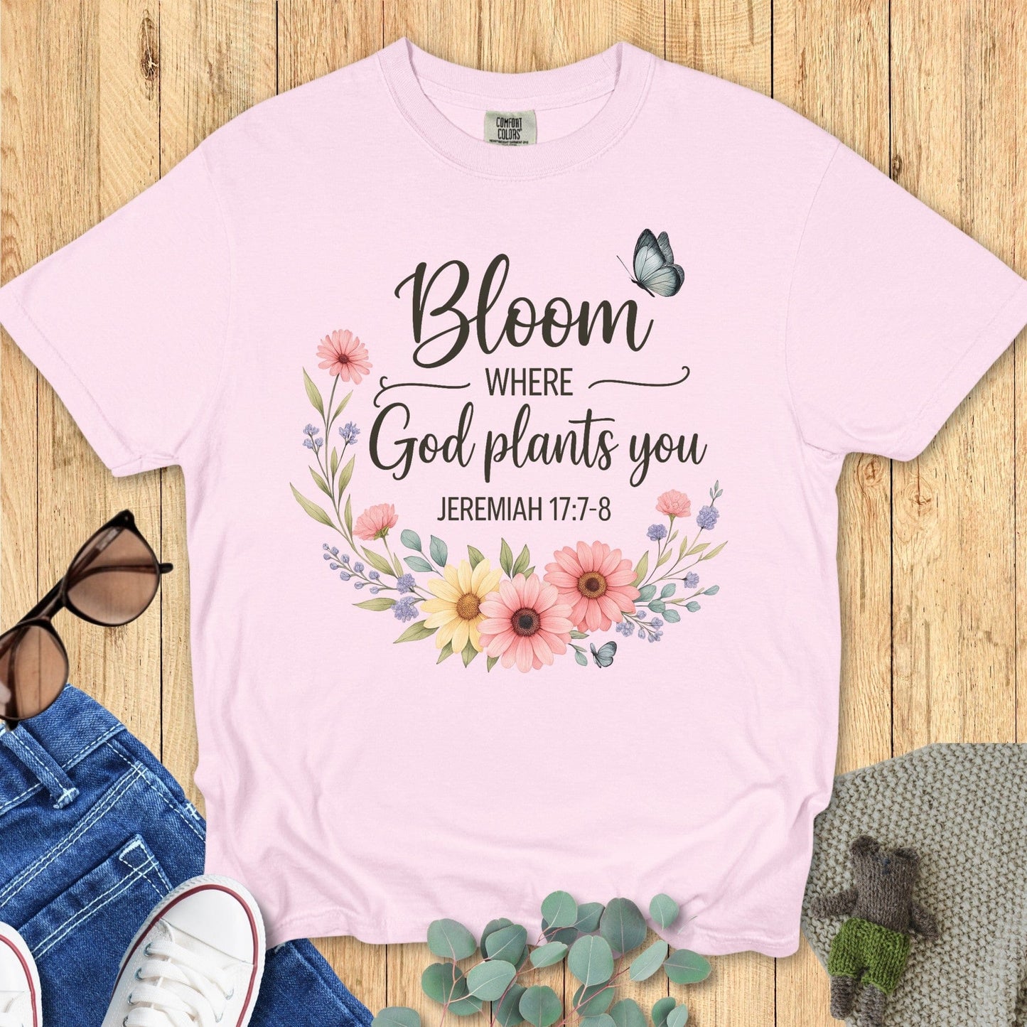 Flatlay of a Comfort Colors 1717 ivory “Bloom Where God Plants You – Jeremiah 17:7-8” t-shirt featuring pastel wildflowers and butterflies. A soft and feminine women’s scripture tee — modern Christian shirt and uplifting faith-based apparel for women, perfect Christian mom gift idea.