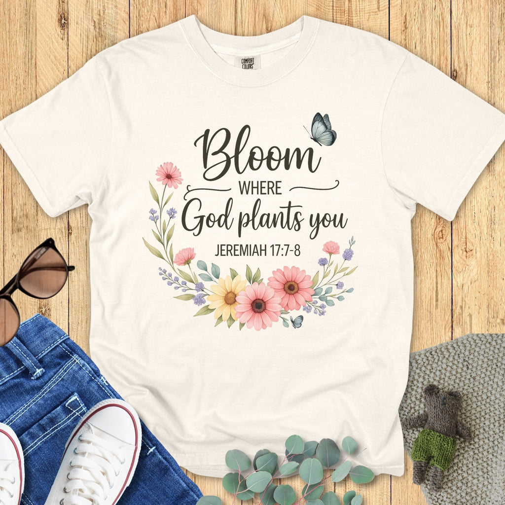 Flatlay of a Comfort Colors 1717 blossom “Bloom Where God Plants You – Jeremiah 17:7-8” t-shirt surrounded by jeans, sneakers, and greenery. A bright, encouraging women’s scripture tee — faith-based apparel for women and Christian mom gift that celebrates growth and faith.