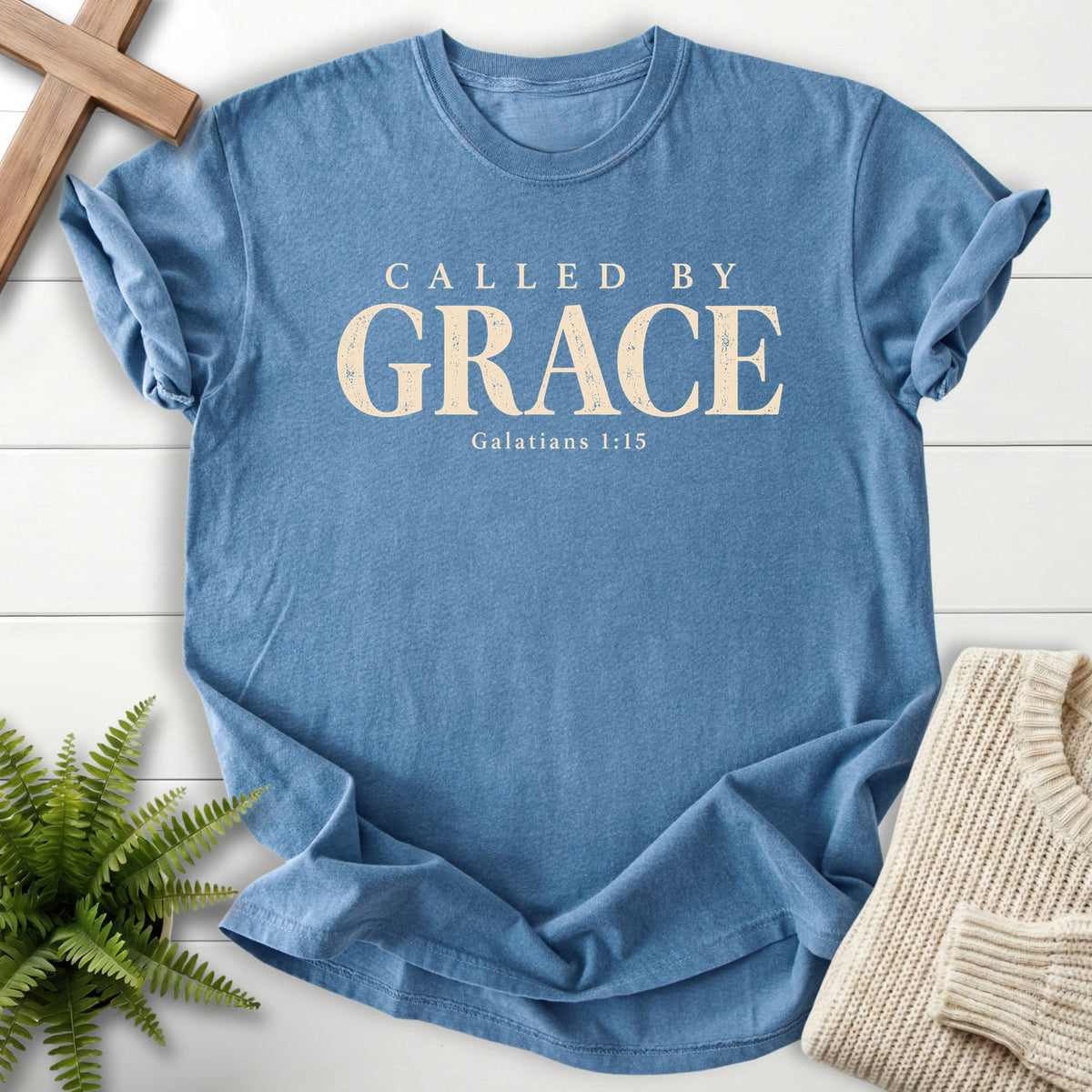 Flat lay of a Blue Jean Christian graphic tee featuring "Called by Grace T-Shirt" Galatians 1:15.