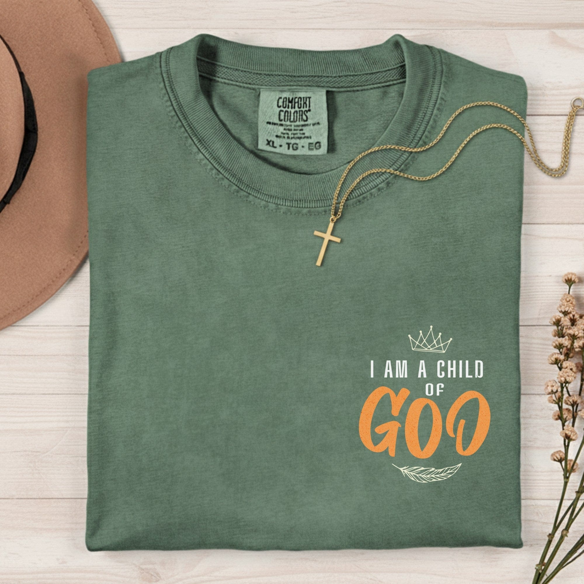 Flatlay of a Comfort Colors 1717 moss “I Am a Child of God” t-shirt featuring elegant crown and feather artwork. A soft women’s scripture tee — meaningful faith-based apparel for women and lovely modern Christian shirt, perfect for Christian mom gift ideas.