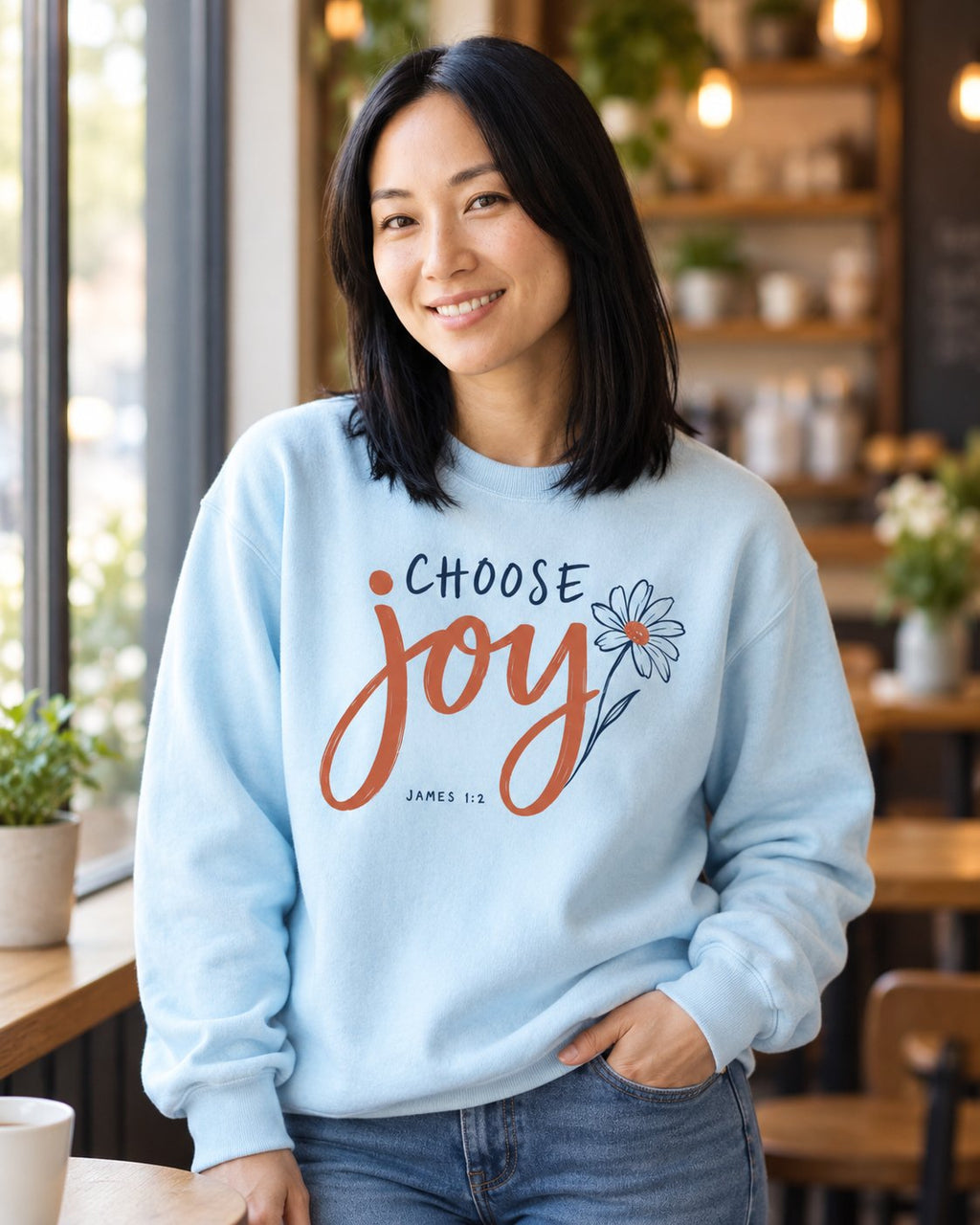 Choose Joy Floral Script, Chambray women's Christian sweatshirt, lifestyle photo in cozy cafe, Choose Joy script lettering with a daisy outline, She Wears Faith