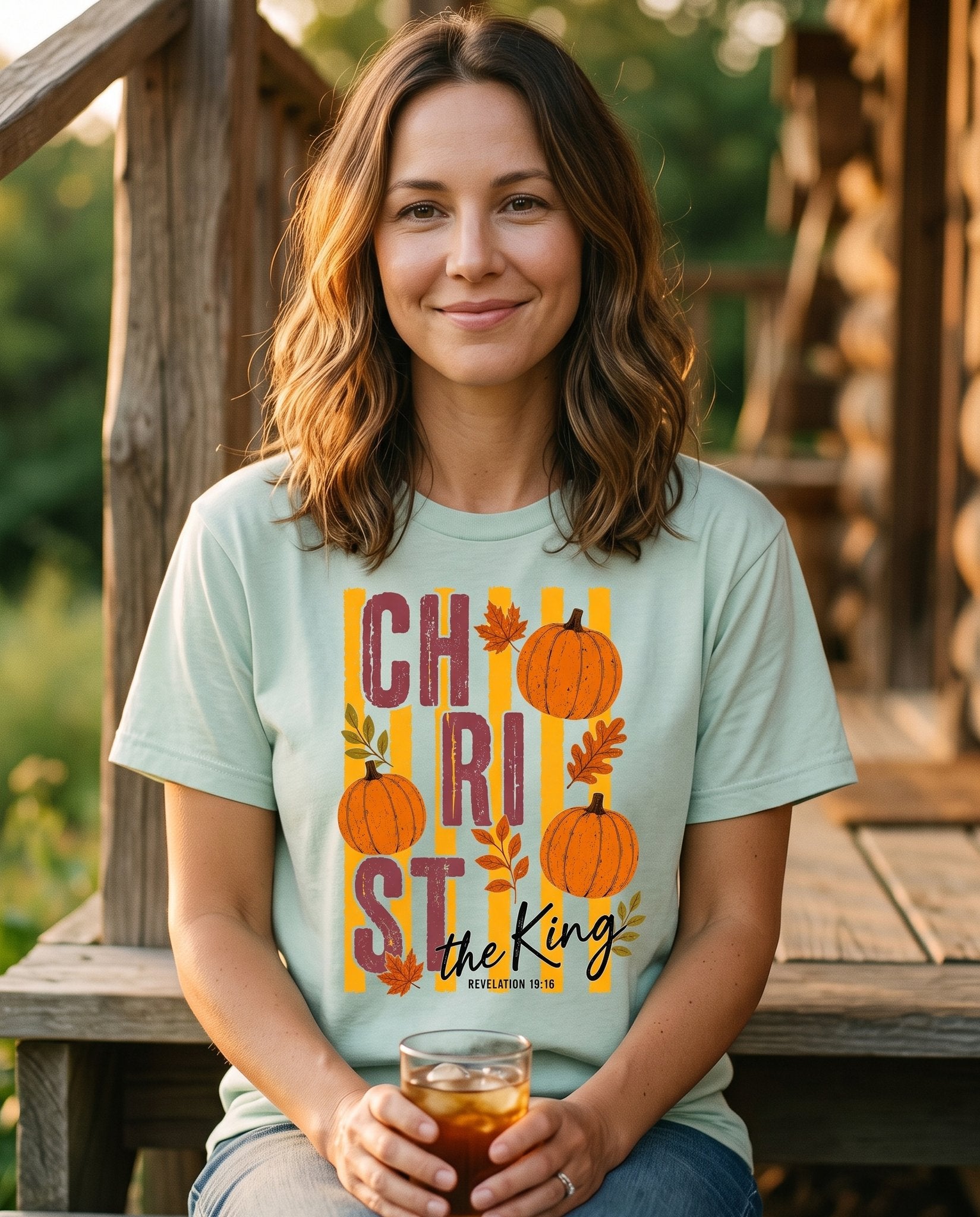 Christ The King Fall – Bay women's Christian tee, lifestyle photo in sunny porch – Bold stacked "CHRIST IS KING" lettering integrated with autumn pumpkin – Revelation 19:16 – She Wears Faith