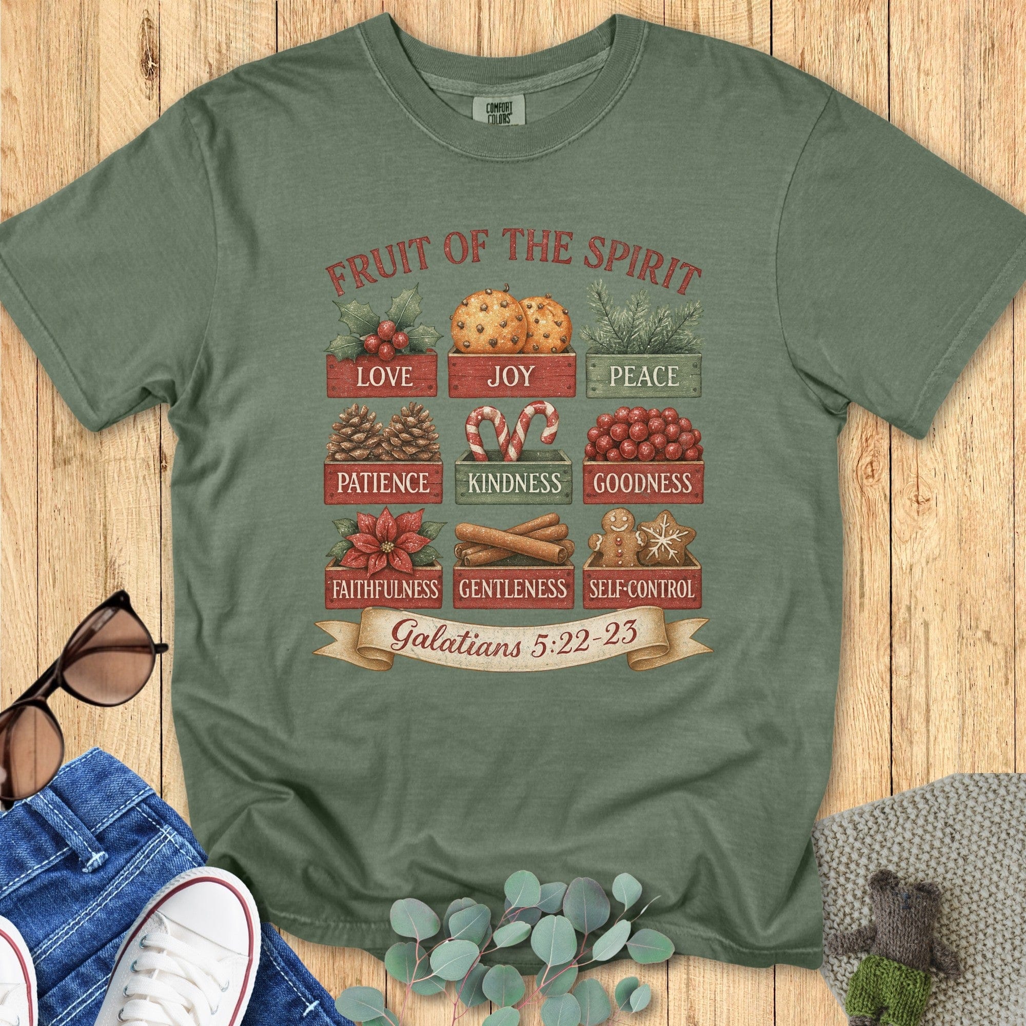Flatlay of a Comfort Colors 1717 moss “Fruit of the Spirit” t-shirt featuring vintage-style Christmas crates with love, joy, peace, patience, kindness, goodness, faithfulness, gentleness, and self-control from Galatians 5:22–23. A festive women’s scripture tee — faith-based apparel for women and modern Christian shirt, thoughtful Christian mom gift idea.