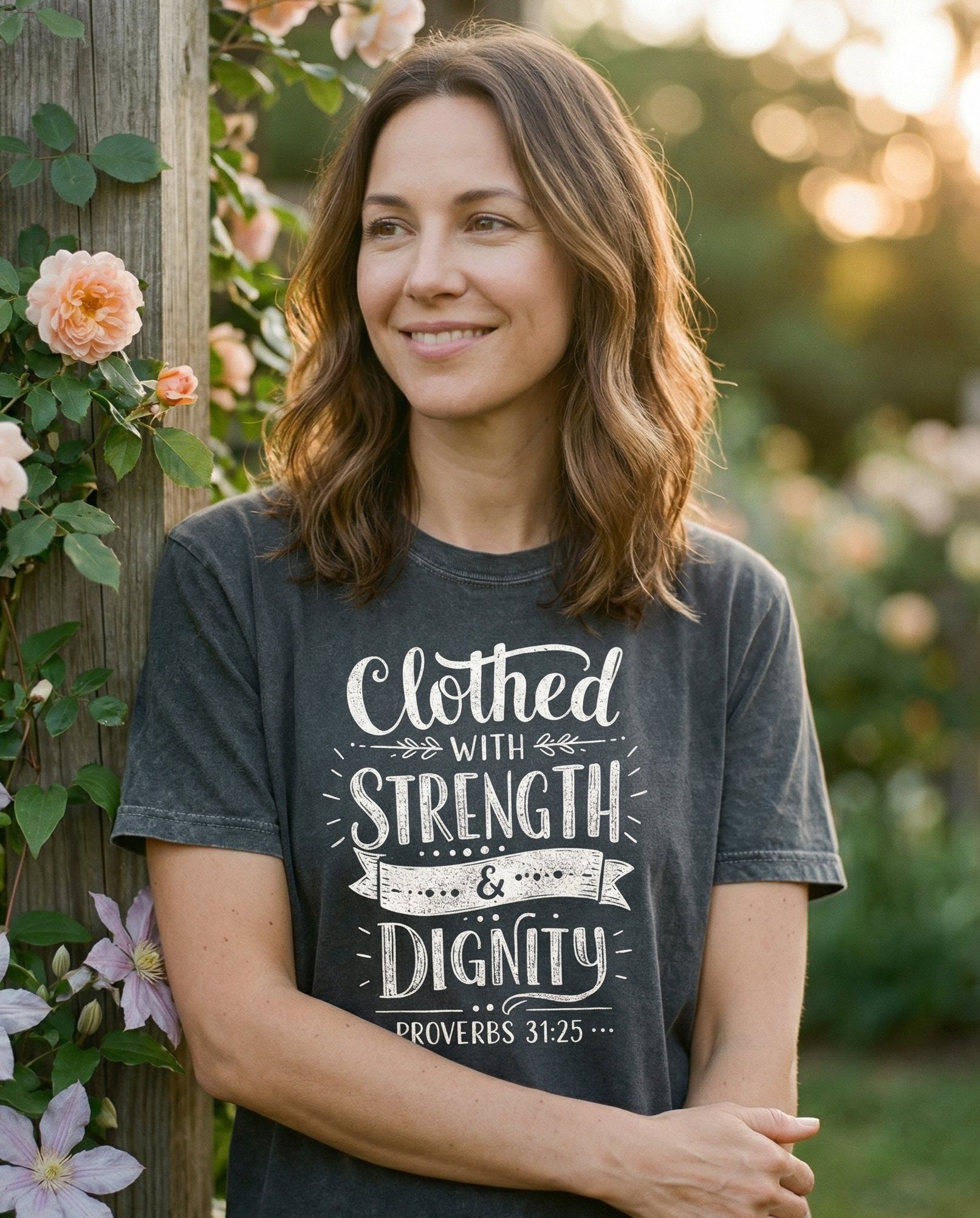 Clothed with Strength T-shirt – Pepper women's Christian tee, lifestyle photo in outdoor garden – Bold mixed typography design reads 'Clothed WITH STRENGTH & Dignity – Proverbs 31:25 – She Wears Faith