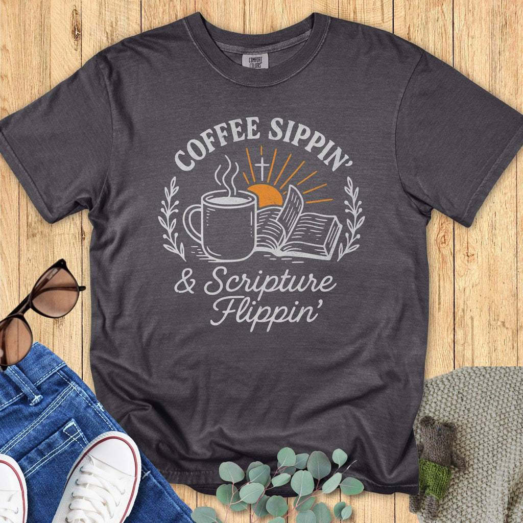 Flatlay of a Comfort Colors 1717 pepper “Coffee Sippin’ & Scripture Flippin’” t-shirt featuring a steaming mug, open Bible, and sunrise graphic. A stylish women’s scripture tee - faith-based apparel for women and modern Christian shirt, thoughtful Christian mom gift idea for coffee and Bible lovers.