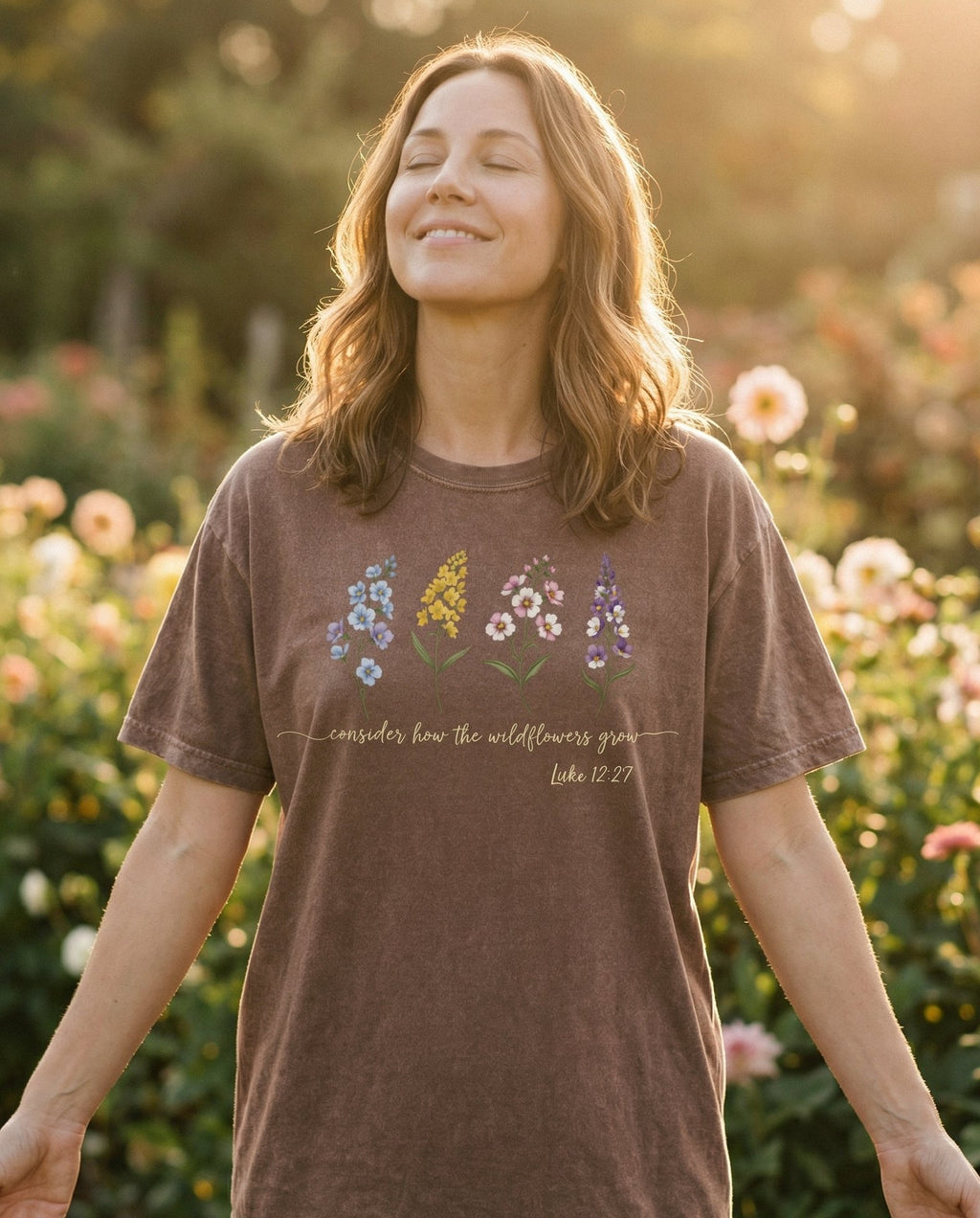 Consider the Wildflowers – Espresso women's Christian tee, lifestyle photo in outdoor garden – Row of four illustrated wildflowers including delphinium – Luke 12:27 – She Wears Faith