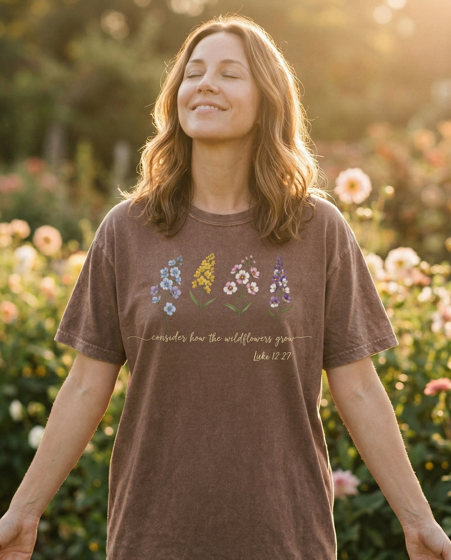 Consider the Wildflowers – Espresso women's Christian tee, lifestyle photo in outdoor garden – Row of four illustrated wildflowers including delphinium – Luke 12:27 – She Wears Faith