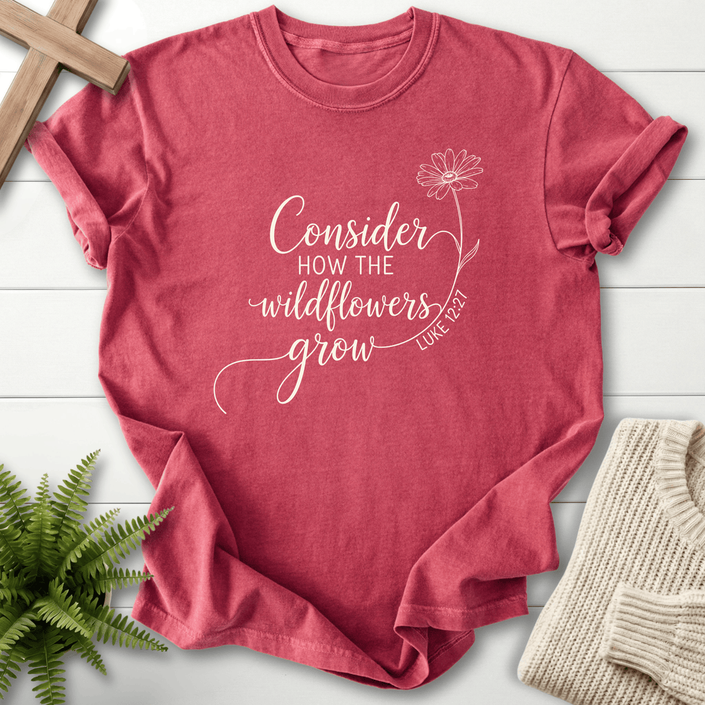 Crimson Christian t-shirt for women with white calligraphy script and a daisy illustration, inspired by Luke 12:27.