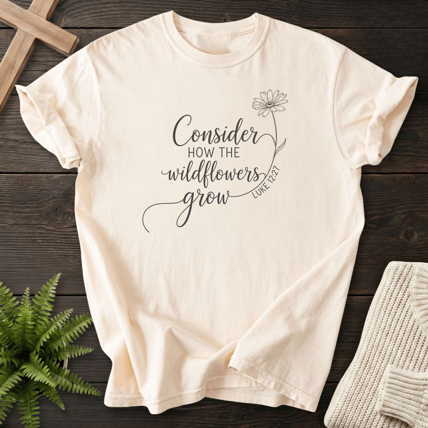 Ivory Christian t-shirt for women with elegant black line art script and a daisy stem, inspired by Luke 12:27.