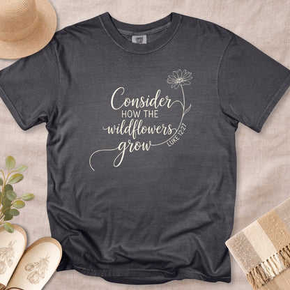 Pepper Grey Comfort Colors 1717 tshirt displaying white script typography and a simple flower line art. A minimalist Christian women tee with the scripture "Consider how the wildflowers grow" (Luke 12:27), perfect for US faith wear collections.