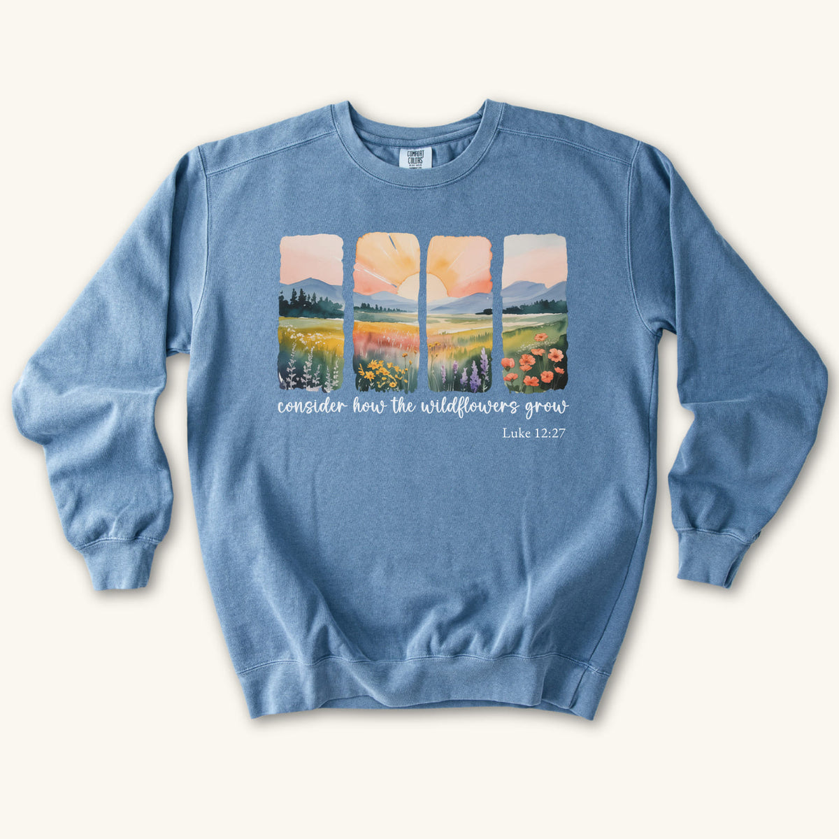 Blue Jean Christian sweatshirt with four painted panels of sunrise over hills and a wildflower meadow, reading consider how the wildflowers grow, Luke 12:27