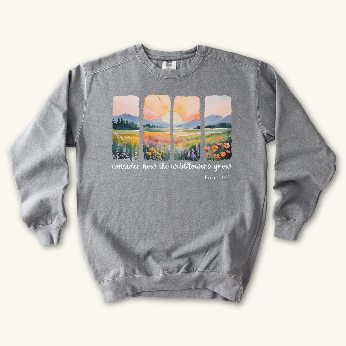 Grey Christian sweatshirt with four painted panels of sunrise over hills and a wildflower meadow, reading consider how the wildflowers grow, Luke 12:27