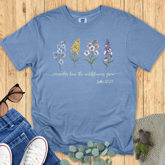 Comfort Colors 1717 Christian women t-shirt in blue jean flat lay. Faith-based design shows four wildflower illustrations with the scripture “Consider how the wildflowers grow – Luke 12:27