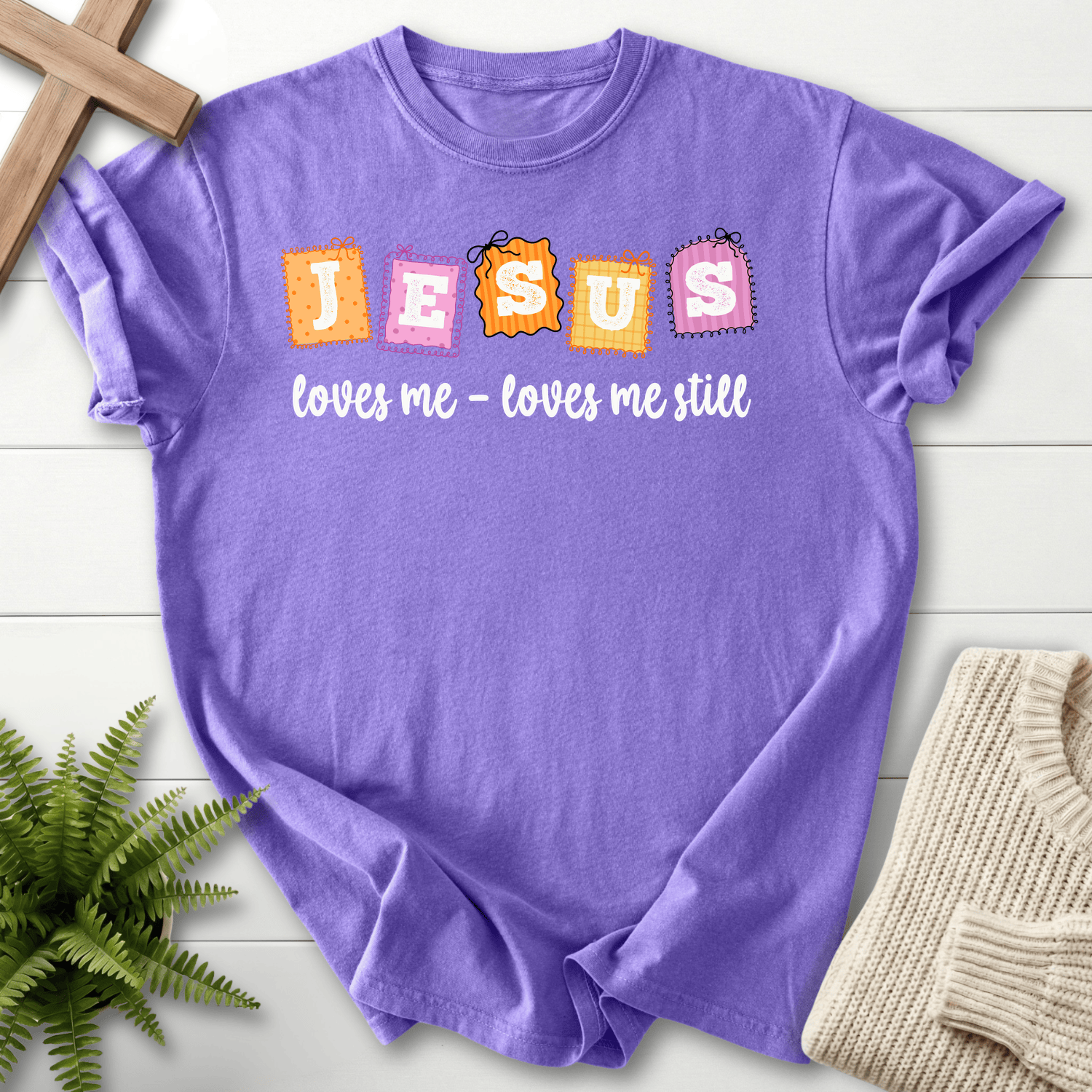 Violet women's Christian t-shirt with playful patchwork "Jesus loves me still" stamp letters