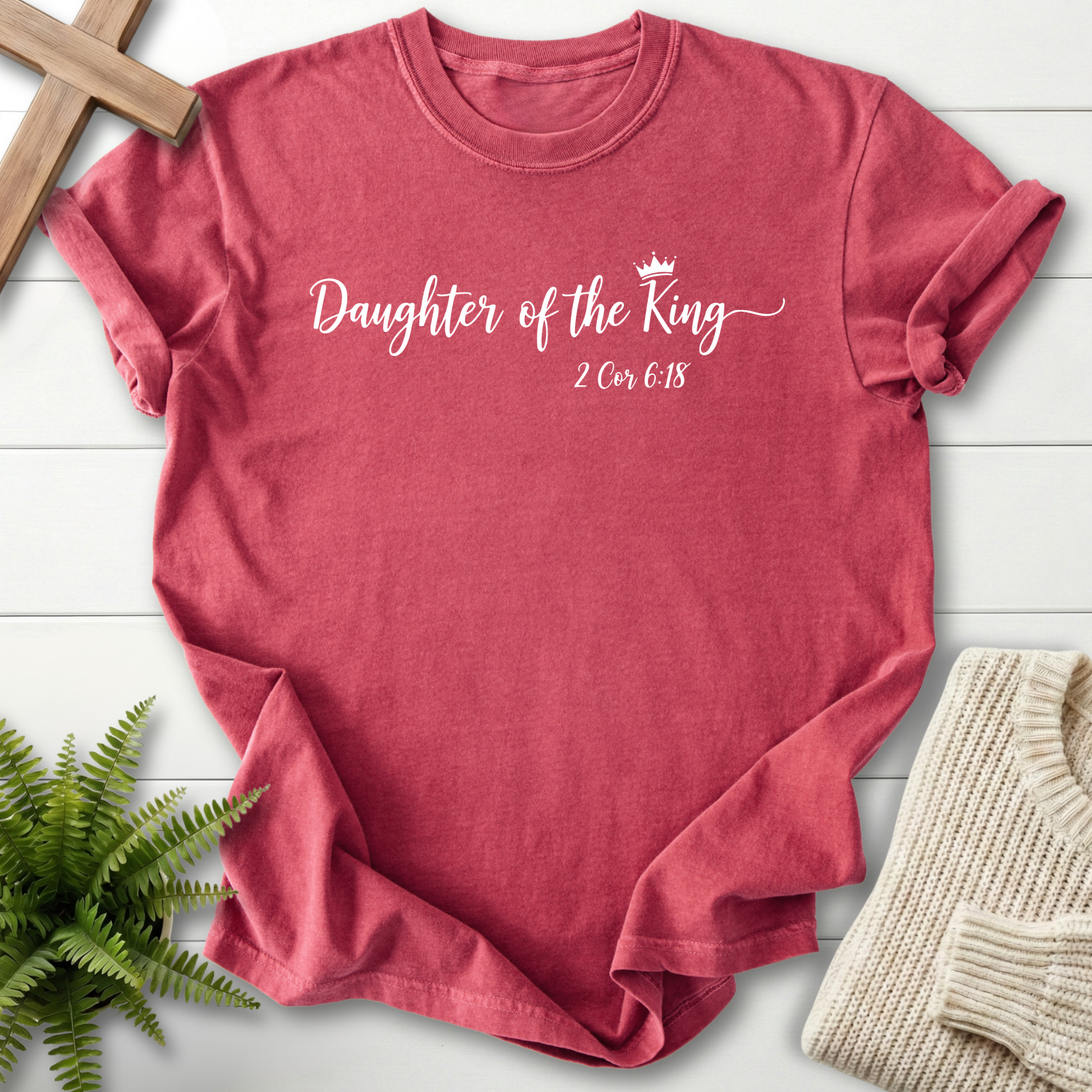 Crimson women's faith t-shirt with elegant white cursive 'Daughter of the King' lettering and a crown icon, inspired by 2 Corinthians 6:18.