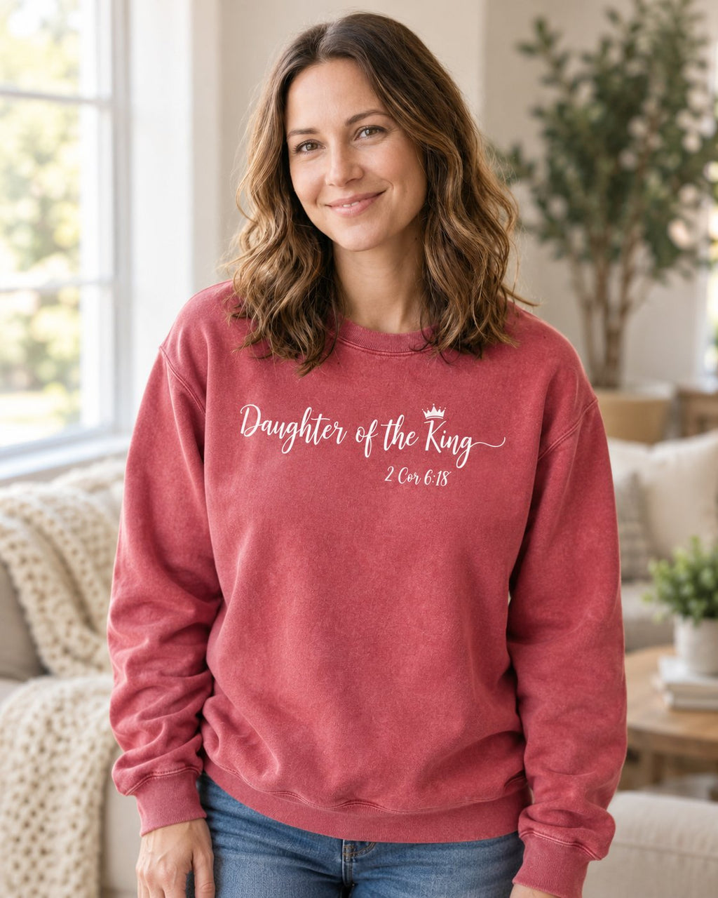 Daughter of the King Script – Crimson women's Christian sweatshirt, lifestyle photo in cozy living room – White script Daughter of the King with a crown – She Wears Faith
