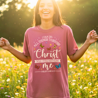 Smiling woman standing in a wildflower field wearing a Comfort Colors 1717 crimson “I Can Do All Things Through Christ Who Strengthens Me – Philippians 4:13” t-shirt. A joyful and inspiring modern Christian shirt that celebrates faith and strength — ideal Christian mom gift idea.