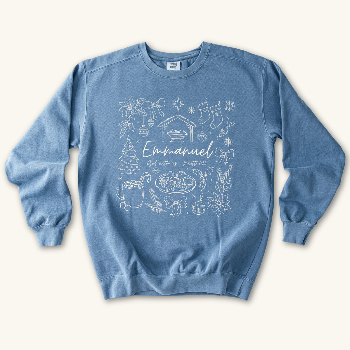 Blue Jean Christian Christmas sweatshirt with Emmanuel God with us script and Matthew 1:23 surrounded by doodles of a manger, stockings, a tree, cocoa and cookies.