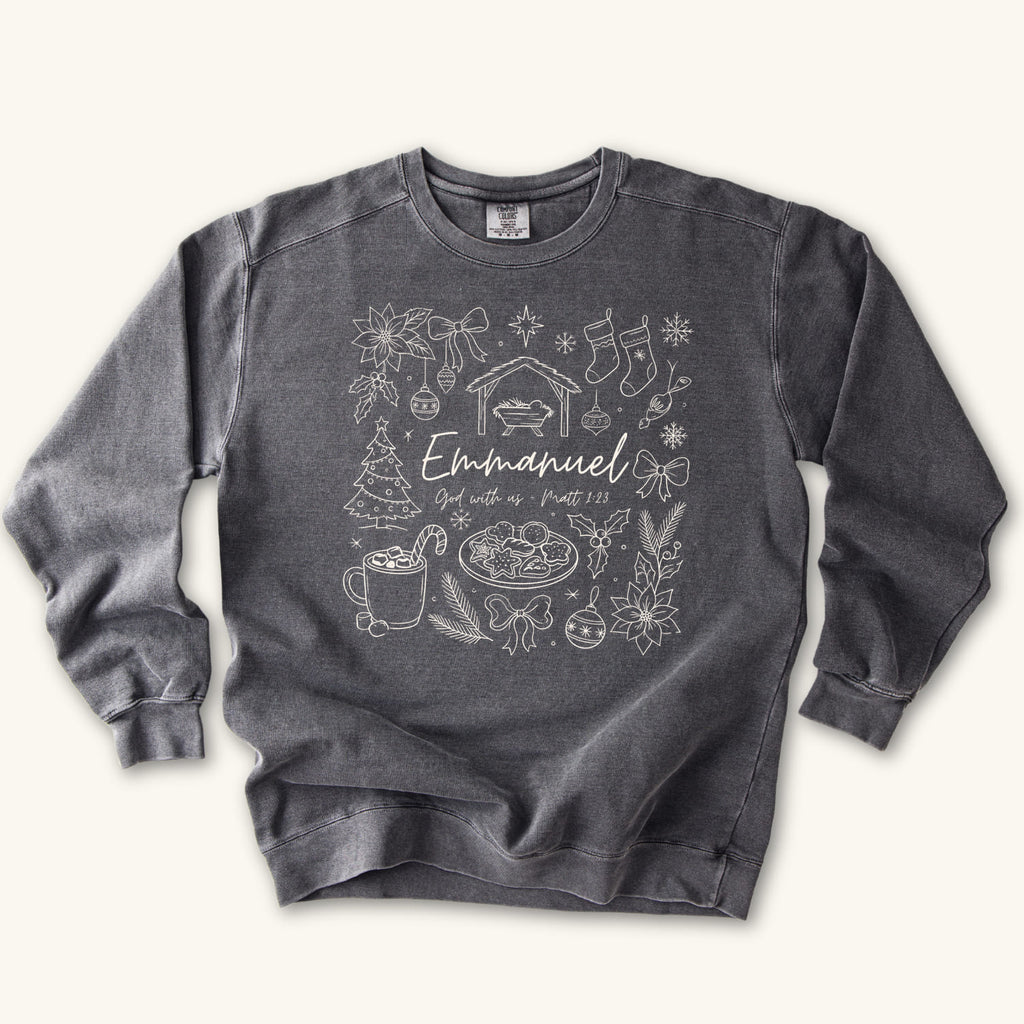Pepper Christian Christmas sweatshirt with Emmanuel God with us script and Matthew 1:23 surrounded by doodles of a manger, stockings, a tree, cocoa and cookies.