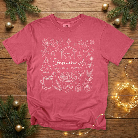 Comfort Colors 1717 crimson Christian women tee featuring a festive Christmas line-art design with the nativity scene, ornaments, bows, stockings, cookies, and the text “Emmanuel – God with us, Matt 1:23.” A soft, garment-dyed holiday faith shirt perfect for US faith wear.
