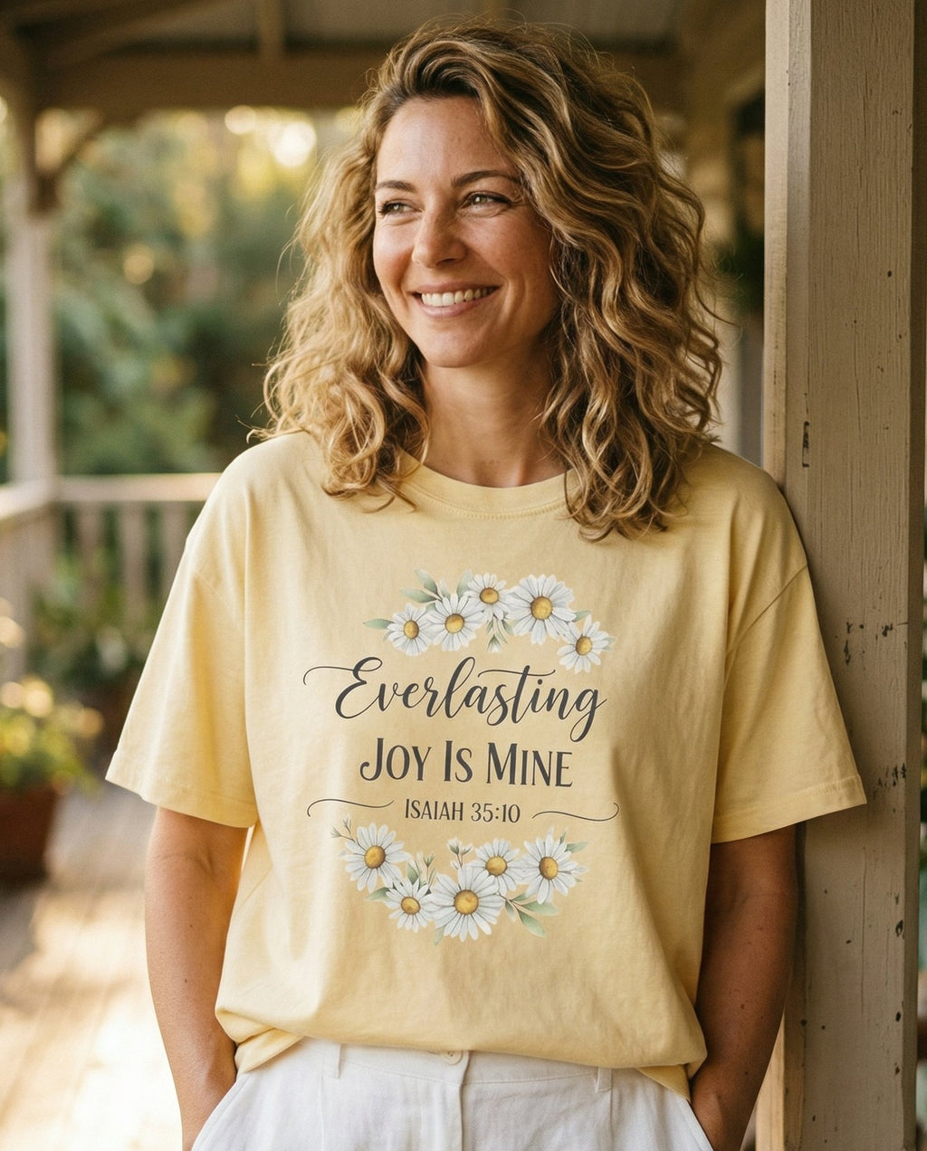 Everlasting Joy – Banana women's Christian tee, lifestyle photo in sunny porch – Watercolor white daisy wreath framing 'Everlasting Joy Is Mine – Isaiah 35:10 – She Wears Faith