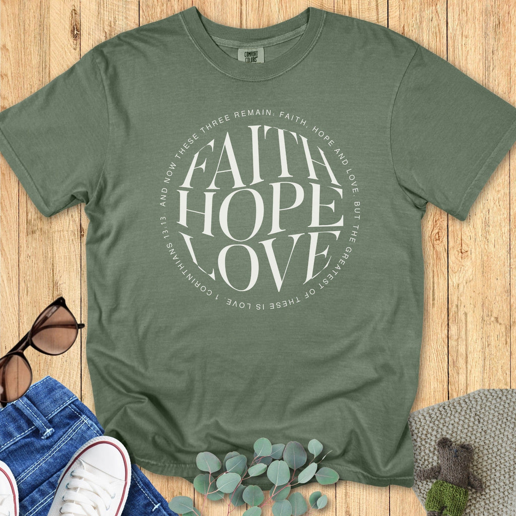 Flatlay of a Comfort Colors 1717 moss “Faith Hope Love” t-shirt featuring 1 Corinthians 13:13 in a circular modern design. A soft women’s scripture tee  - faith-based apparel for women and modern Christian shirt, meaningful Christian mom gift idea celebrating faith, hope, and love.