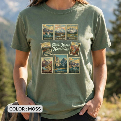 Woman standing outdoors wearing a Moss Green Comfort Colors 1717 tshirt featuring vintage national park stamps (Yosemite, Rocky Mountain, etc.). A nature-themed Christian women tee with the inspirational text "Faith Moves Mountains," perfect for adventure lovers and US faith wear collections.