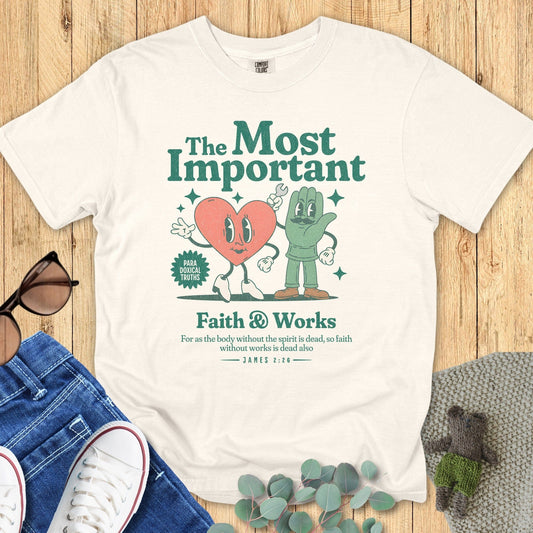 Flatlay of a Comfort Colors 1717 ivory “Faith & Works” t-shirt with vintage cartoon-style heart and hand design referencing James 2:26. A fun women’s scripture tee -  faith-based apparel for women and modern Christian shirt, thoughtful Christian mom gift idea blending humor and truth.